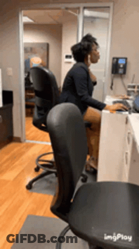 A Woman Is Sitting At A Desk In An Office Using A Computer GIF