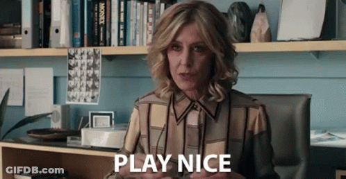 A Woman Is Sitting At A Desk In Front Of A Bookshelf And Saying Play Nice . GIF