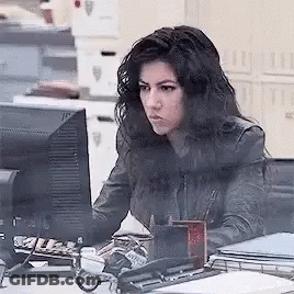 A Woman Is Sitting At A Desk In Front Of A Computer Screen . GIF