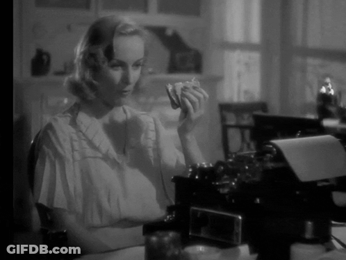 A Woman Is Sitting At A Desk In Front Of A Typewriter And Holding Something In Her Hand GIF