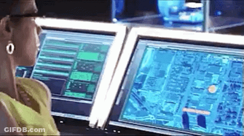 A Woman Is Sitting At A Desk In Front Of Two Computer Monitors . GIF