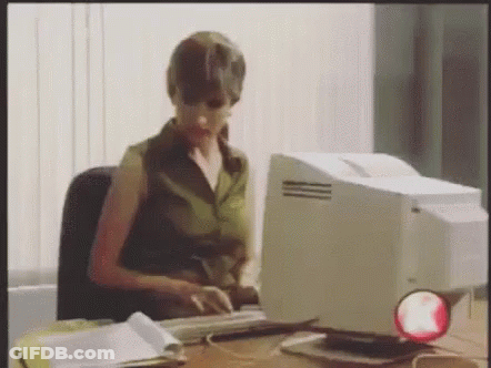 A Woman Is Sitting At A Desk Typing On A Computer . GIF