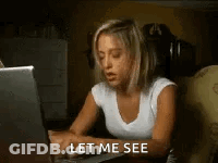 A Woman Is Sitting At A Desk Using A Laptop Computer And Says `` Let Me See '' . GIF