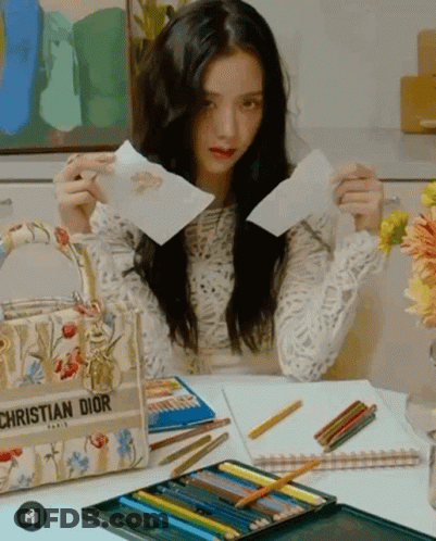 A Woman Is Sitting At A Desk With A Christian Dior Bag GIF