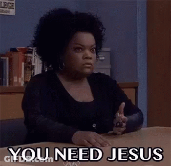A Woman Is Sitting At A Desk With A Gun In Her Hand And The Words `` You Need Jesus '' Written On Her Face . GIF