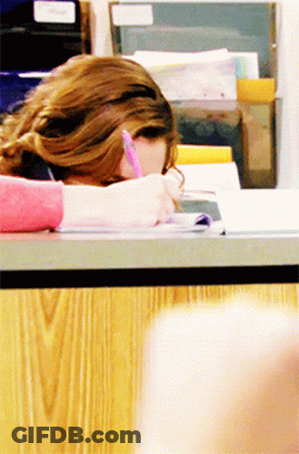 A Woman Is Sitting At A Desk With Her Head Down Writing In A Notebook GIF