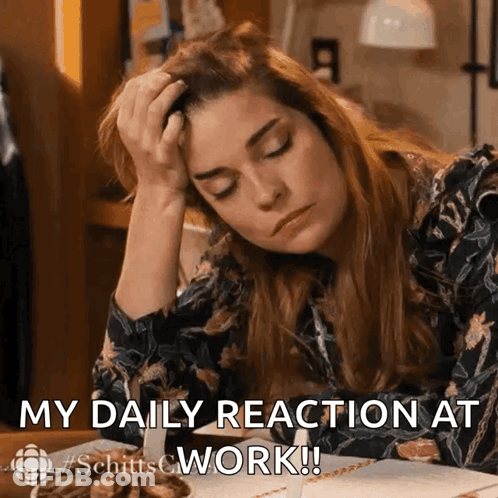 A Woman Is Sitting At A Desk With Her Head In Her Hand And The Words " My Daily Reaction At Work " Below Her GIF
