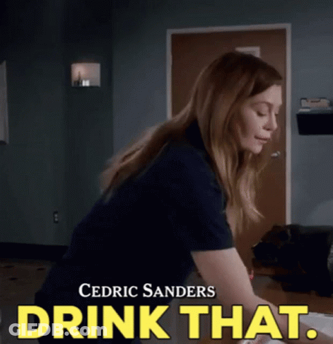 A Woman Is Sitting At A Desk With The Words Drink That Written On The Bottom . GIF