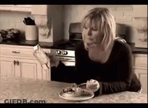A Woman Is Sitting At A Kitchen Counter With A Plate Of Food And A Newspaper . GIF