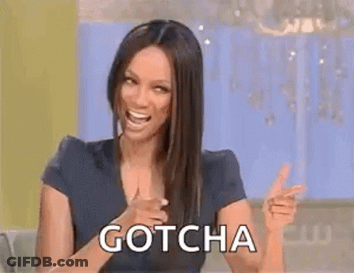 A Woman Is Sitting At A Table And Pointing At The Camera While Laughing And Saying `` Gotcha '' . GIF