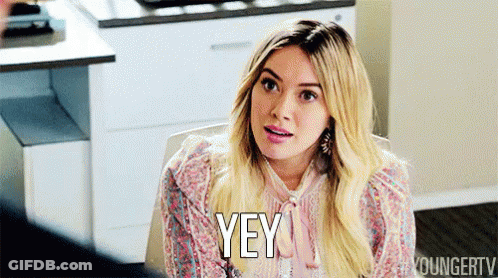 A Woman Is Sitting At A Table And Saying Yey GIF