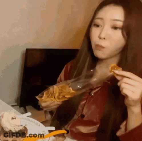 A Woman Is Sitting At A Table Eating A Bag Of Chips GIF