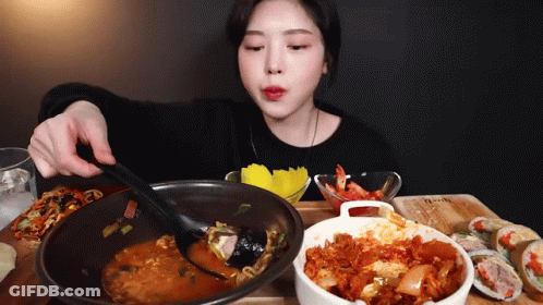 A Woman Is Sitting At A Table Eating A Bowl Of Food GIF