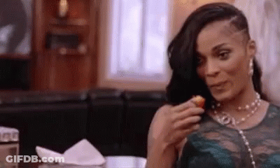 A Woman Is Sitting At A Table Eating A Fried Food . GIF