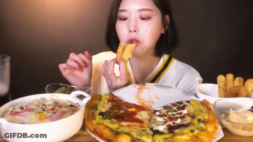 A Woman Is Sitting At A Table Eating A Pizza And French Fries GIF