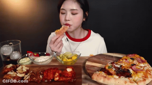 A Woman Is Sitting At A Table Eating A Slice Of Pizza . GIF