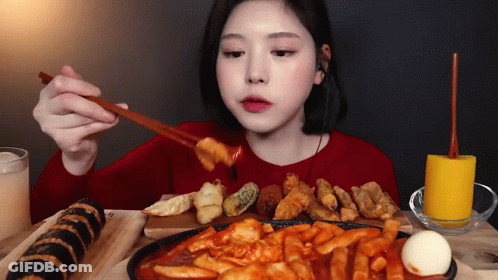 A Woman Is Sitting At A Table Eating A Variety Of Foods With Chopsticks . GIF