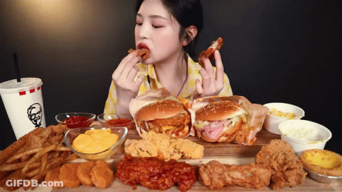 A Woman Is Sitting At A Table Eating A Variety Of Fried Food Including A Kfc Drink GIF