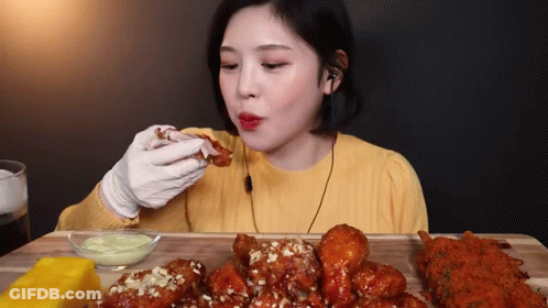 A Woman Is Sitting At A Table Eating Fried Chicken And Cheese . GIF