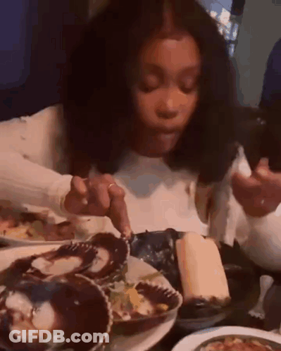 A Woman Is Sitting At A Table Eating Oysters With A Fork . GIF