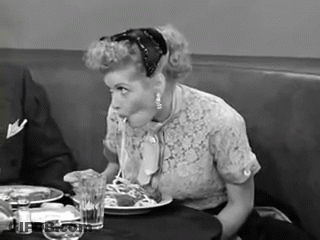 A Woman Is Sitting At A Table Eating Spaghetti With A Spoon GIF