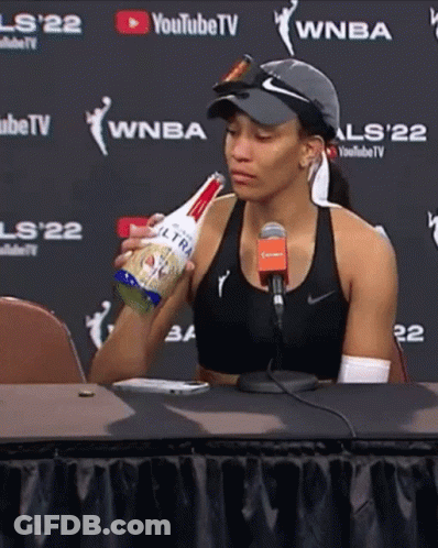 A Woman Is Sitting At A Table Holding A Bottle Of Ultra Light Beer GIF