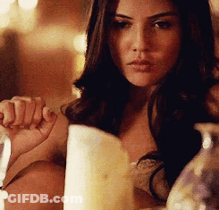A Woman Is Sitting At A Table Holding A Candle . GIF