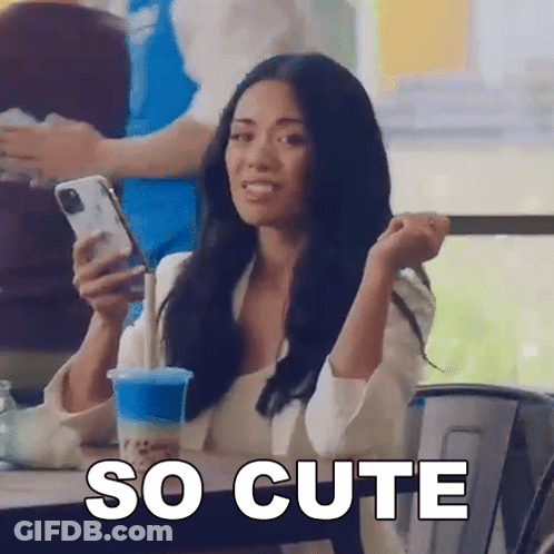 A Woman Is Sitting At A Table Holding A Cell Phone And A Cup Of Blue Liquid . GIF