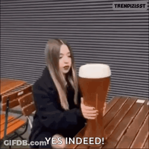 A Woman Is Sitting At A Table Holding A Very Large Glass Of Beer . GIF