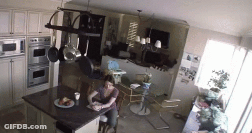 A Woman Is Sitting At A Table In A Kitchen Reading A Book GIF