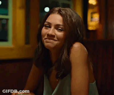 A Woman Is Sitting At A Table In A Restaurant Smiling At The Camera . GIF