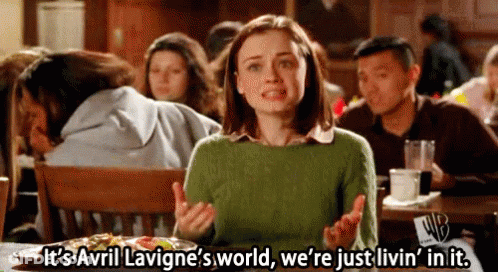 A Woman Is Sitting At A Table In A Restaurant Talking About Avril Lavigne 'S World GIF