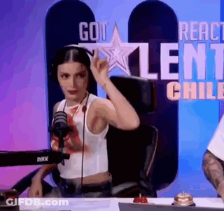A Woman Is Sitting At A Table In Front Of A Microphone And A Sign That Says Got Talent Chile . GIF