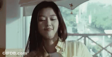 A Woman Is Sitting At A Table In Front Of A Window And Smiling . GIF