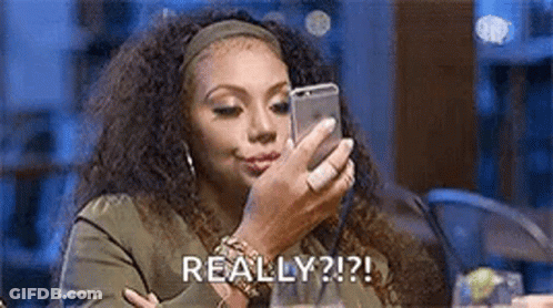 A Woman Is Sitting At A Table Looking At A Cell Phone . GIF