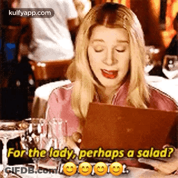 A Woman Is Sitting At A Table Looking At A Menu And Asking For A Salad . GIF