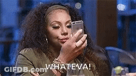 A Woman Is Sitting At A Table Looking At Her Cell Phone And Saying Whateva . GIF
