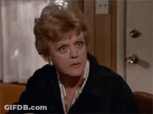 A Woman Is Sitting At A Table Making A Funny Face And Looking At The Camera . GIF