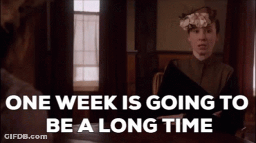 A Woman Is Sitting At A Table With A Book In Her Hand And A Flower In Her Hair While Talking To Another Woman . GIF