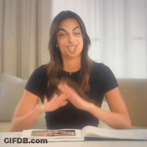 A Woman Is Sitting At A Table With A Book On It GIF