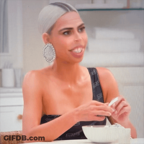 A Woman Is Sitting At A Table With A Bowl Of Cereal And A Spoon GIF