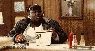 A Woman Is Sitting At A Table With A Bucket Of Town Chicken In Front Of Her GIF