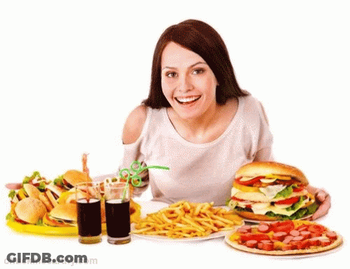 A Woman Is Sitting At A Table With A Bunch Of Food Including A Hamburger French Fries And A Pizza GIF