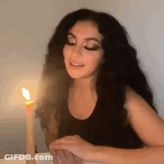 A Woman Is Sitting At A Table With A Candle In Front Of Her . GIF