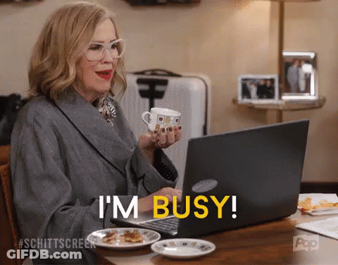 A Woman Is Sitting At A Table With A Cup Of Coffee And A Laptop And Says I 'M Busy GIF