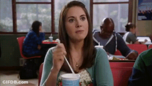A Woman Is Sitting At A Table With A Cup Of Milkshake GIF