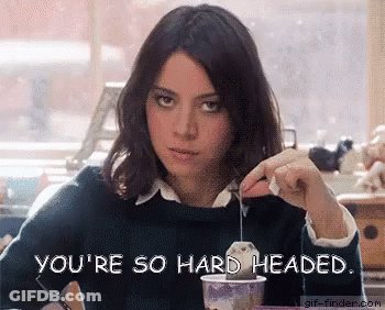 A Woman Is Sitting At A Table With A Cup Of Tea And The Words You 'Re So Hard Headed On The Bottom GIF