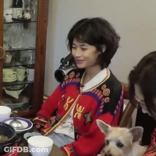 A Woman Is Sitting At A Table With A Dog And Two Women . GIF