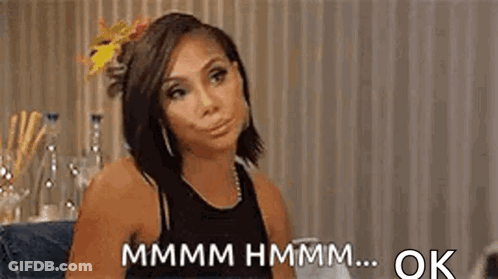A Woman Is Sitting At A Table With A Flower In Her Hair And Making A Face . GIF