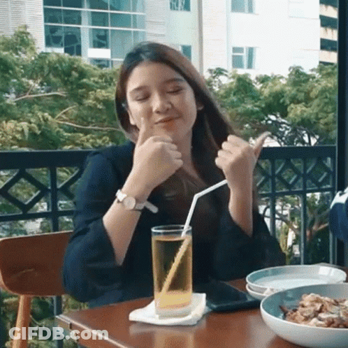 A Woman Is Sitting At A Table With A Glass Of Beer And A Straw . GIF